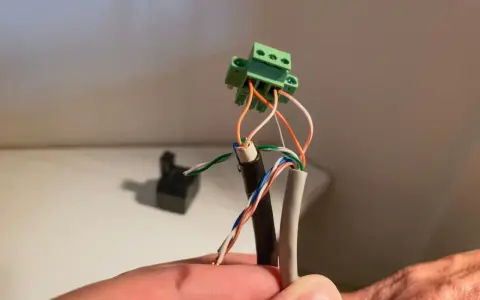 Connexion de fils électriques colorés à un connecteur vert. Un petit point lumineux attire l'œil sur le fil blanc.