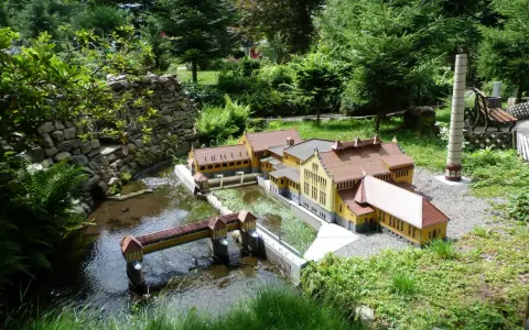 Miniaturowa zabudowa z mostkiem i rzeką, jak w parkach miniatur w Polsce.