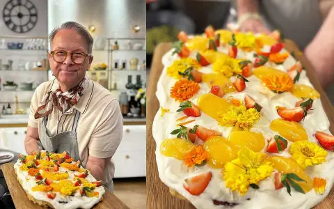 Glad kock visar upp en vacker påsktårta i långpanna, dekorerad med jordgubbar, aprikoser och gula blommor.