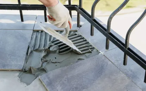 Układanie płytek na balkonie. Zastanawiasz się, ile kosztuje remont balkonu w bloku? Prace obejmują fugowanie i klejenie.