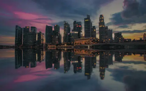 Wieżowce w Singapurze odbijają się w wodzie o zachodzie słońca. To miasto-państwo, gdzie leży Singapur, zachwyca nowoczesną architekturą.