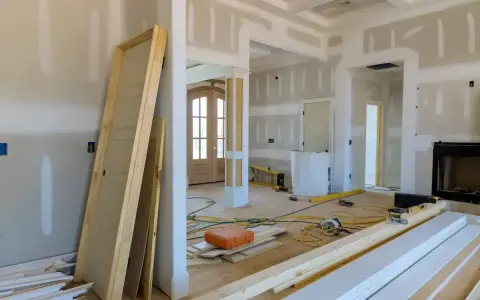 Wnętrze w trakcie przebudowy. Widać nowe drzwi, materiały budowlane, narzędzia i przygotowane do montażu listwy przypodłogowe.