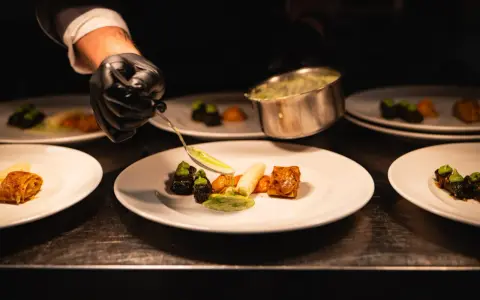 Szef kuchni precyzyjnie serwuje sos, dbając o zasady serwowania dań w stylu "fine dining" na dużych imprezach.