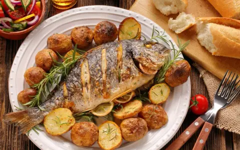 Pieczona ryba z ziemniakami, cytryną i rozmarynem na talerzu.