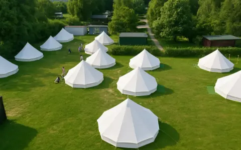 Wioska namiotów typu bell, idealna na glamping. Kilka osób spaceruje po zielonej trawie między białymi, stożkowymi konstrukcjami.