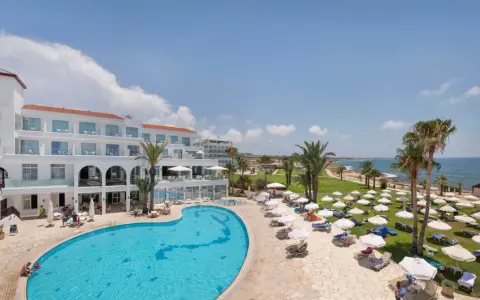 Słoneczny dzień w Akti Beach Village Resort. Basen, leżaki, palmy i morze - idealne miejsce na wakacje.