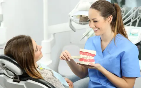 Uśmiechnięta higienistka stomatologiczna pokazuje pacjentce, jak prawidłowo szczotkować zęby na modelu szczęki.