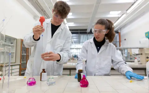 Ragazzi in camice bianco e occhiali protettivi eseguono esperimenti in laboratorio, un passo verso il loro futuro diploma perito chimico.