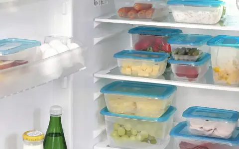 Frigo organizzato con contenitori trasparenti: carote, formaggio, cetrioli, uva, affettati. Un esempio di come organizzare il frigo per conservare al meglio gli alimenti.