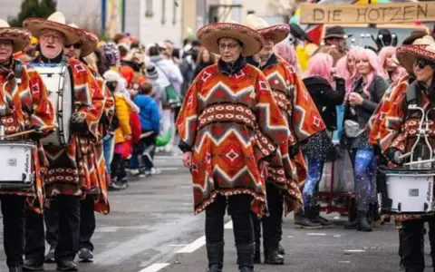Menschen in bunten Ponchos und Sombreros marschieren mit Trommeln. Sie feiern Fasching, eine Zeit voller Freude und Verkleidungen.