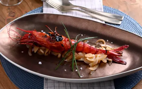 Un langostino rojo a la parrilla, servido sobre cebolla caramelizada y adornado con cebollino. Un plato que evoca la pregunta: ¿qué son los carabineros?