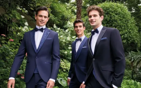 Tre eleganti sposo e testimoni in abiti scuri, sorridono in un giardino lussureggiante.