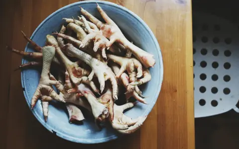 Miseczka pełna kurzych łapek, gotowych do przygotowania dla psa. Naturalny przysmak dla czworonoga.