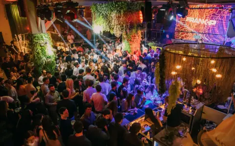 Menschen tanzen und feiern in einem belebten Club in Lissabon. Grüne Pflanzen und Lichter schaffen eine lebendige Atmosphäre.