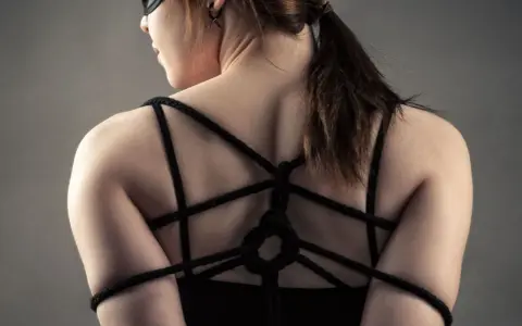 Kobieta w masce z przepaską na oczach, z rękami związanymi sznurkiem na plecach. To może być początek przygody z bdsm dla początkujących.