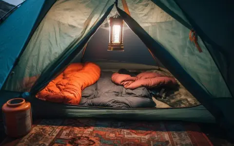 Wnętrze namiotu gotowe do spania. Dwa śpiwory, pomarańczowy i brązowy, czekają na noc. Lampion rzuca ciepłe światło.