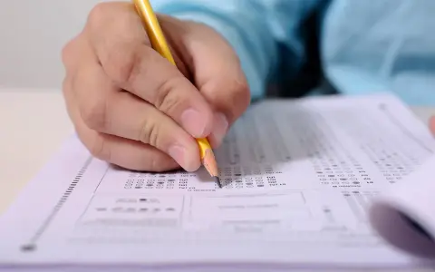 Ręka z ołówkiem wypełnia arkusz testowy. Przygotowanie do egzaminu telc b2 angielski przykładowe testy.