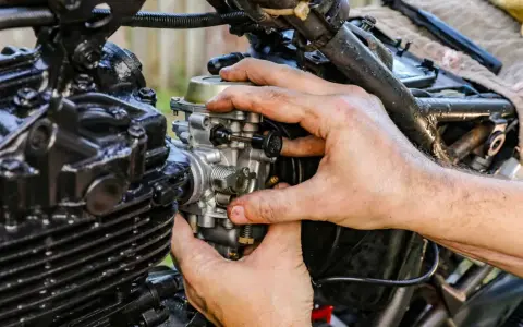 Ręce mechanika regulują gaźnik motocykla, pokazując, jak działa ssanie.