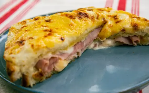Croque Monsieur gratinado con queso derretido y jamón, servido en plato azul.