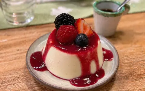 Cremige Panna Cotta mit Beeren und rotem Fruchtsirup auf einem Teller.