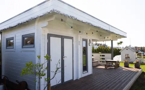 Una cabaña de madera con terraza, ideal para hacer una habitación en una terraza. Luces decorativas cuelgan del techo.