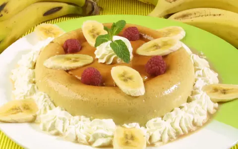Delicioso flan de plátano adornado con rodajas de plátano, frambuesas y crema batida. Un postre perfecto para cualquier ocasión.
