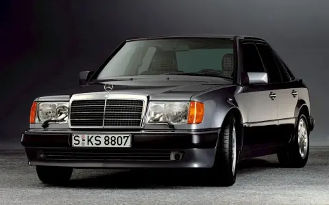 Klasyczny Mercedes W124 w ciemnym kolorze, z charakterystyczną atrapą chłodnicy i reflektorami. Ten model słynie z niezawodnych silników.