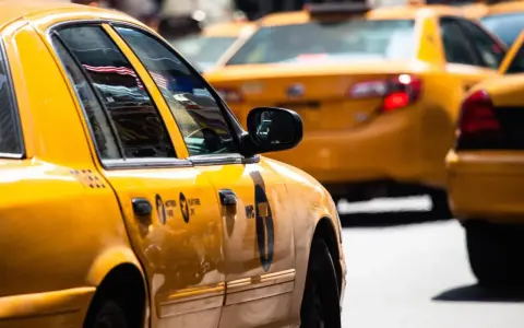 Gelbe Taxis in den USA, ein ikonischer Anblick. Die Spiegelung der US-Flagge im Fenster des vorderen Taxis.
