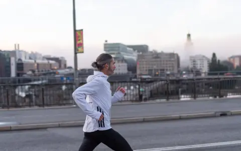 Man med hästsvans springer på en bro i Stockholm, klädd i adidas halvmarathon-kläder.
