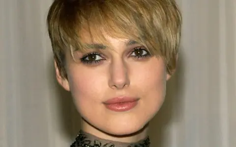Primo piano di una donna con capelli biondi e tagli corti belli, trucco occhi marcato e un choker decorato.