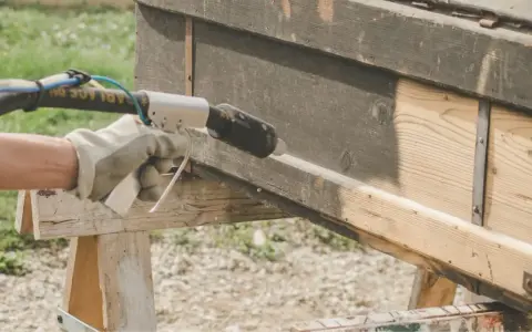 Main tenant en décapeur thermique pour enlever peinture sur bois. Le bois brut apparaît sous la couche sombre.