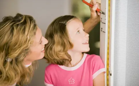 Mama mierzy córkę, która z zaciekawieniem patrzy na miarkę. Czyżby zastanawiała się, dlaczego dziecko nie rośnie tak szybko, jak by chciała?