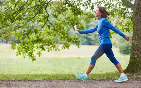 Femme souriante en tenue de sport bleue, profitant de 30 minutes de marche rapide par jour dans un parc verdoyant.