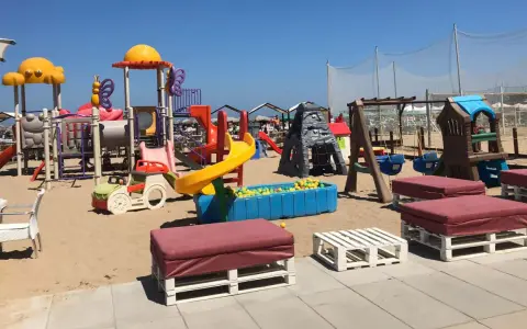 Area giochi per bambini sulla sabbia, con scivoli, altalene e piscina di palline. Un angolo di divertimento al Regina Beach Cattolica.