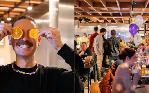 Hombre sonriente con rodajas de naranja en los ojos, en un bar con licencia de bar sin cocina, gente en mesas y globos.