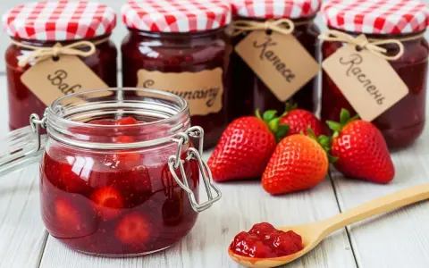 Bocaux de confiture de fraise faits maison, avec des fraises fraîches et une cuillère remplie de confiture.