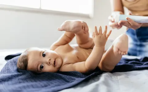 Uroczy noworodek leży na granatowym kocyku, podnosząc nóżki. Mama przygotowuje się do masażu brzuszka, by ulżyć mu w **gazach u noworodka**.
