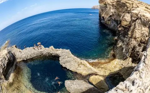 Ludzie kąpią się w naturalnym basenie skalnym, znanym jako blue hole, otoczonym klifami i turkusowym morzem.