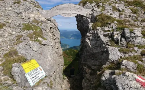 Himmelspforte am Schafberg: Ein Felsentor mit Holzinschrift, das den Blick auf einen See freigibt. Ein Wanderer steht im Durchgang.