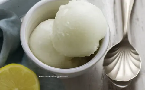 Coppetta di sorbetto al limone, fresca e dissetante, con limone fresco e cucchiaio decorato.