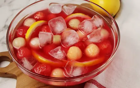 Erfrischende melonenbowle ohne alkohol mit Eiswürfeln, Melonenbällchen und Zitronenscheiben in einer Glasschüssel.
