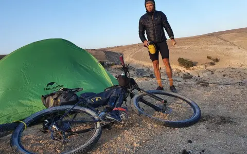 Mann mit Fahrrad und Zelt in bergiger Landschaft, bereit für neue **biking trails**.
