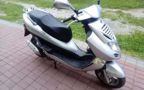 Srebrny skuter Kymco Bet&Win 50 stoi na chodniku z kostki brukowej.
