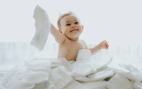 Uśmiechnięty bobas otoczony stertą pieluch. Zastanawiasz się, jakie pieluchy dla noworodka będą najlepsze?
