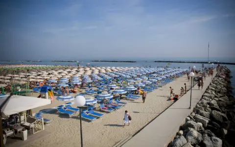 Spiaggia affollata a Gatteo Mare centro, con file di ombrelloni e lettini, gente che passeggia sul molo e si gode il sole.