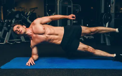 Un homme musclé réalise un gainage planche sur un tapis bleu dans une salle de sport.