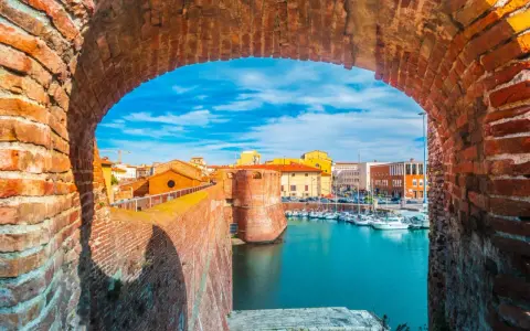 Widok na port w Livorno przez ceglany łuk. Widać łodzie, budynki i fortyfikacje. Idealne miejsce, by zobaczyć Livorno.