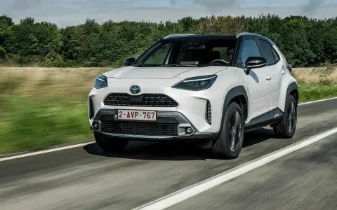 Biały Toyota Yaris Cross jedzie po drodze, otoczony zielenią.