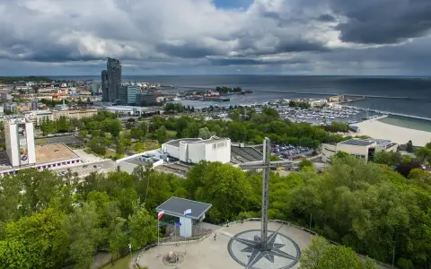 Gdynia co zobaczyć: pomnik z różą wiatrów i krzyżem na wzgórzu, w tle port, plaża i drapacze chmur.