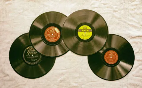 Vier alte Schallplatten liegen auf einer Leinwand. Eine davon hat ein gelbes MGM-Label, die anderen sind von Victrola und Victor. Sie erinnern an die Anfänge des Rocken Roll.